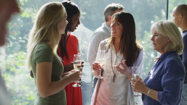 Diverse group of friends chatting & drinking wine at party in contemporary home