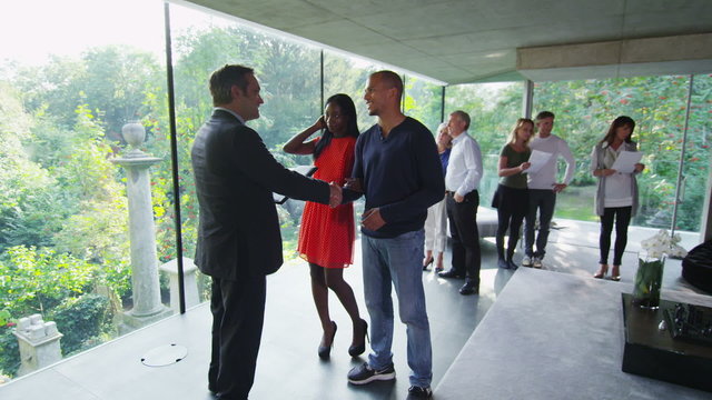 Young Couple Talking To Estate Agent At Open Viewing Of Luxury Modern Home