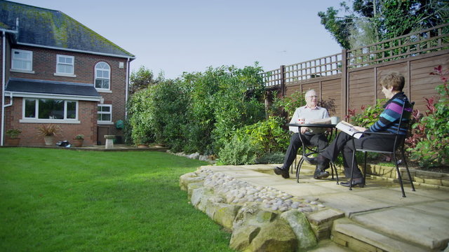 Mature couple of retirement age spend time together sitting in their garden