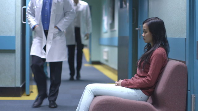 Worried Young Woman Sitting Alone In A Hospital Waiting Area Waits For News.