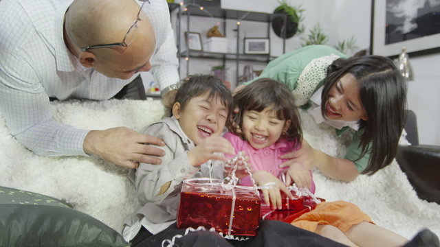 A young brother and sister are surprised by their parents with gifts in shiny red wrapping paper.