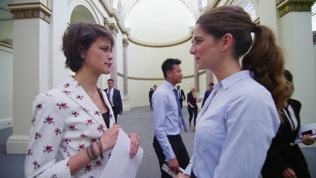 Young female business delegates stand and chat in busy conference building