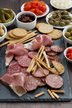 Assorted meat snacks and pickles on a blackboard, vertical