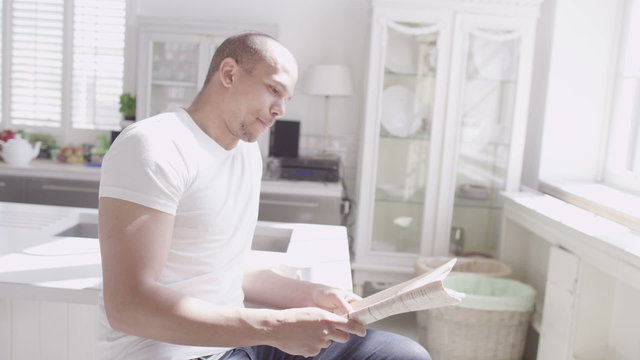 Handsome young man relaxing with a newspaper in his light and elegant home