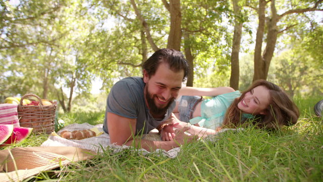 Guy tickling his laughing girlfriend at a park picnic