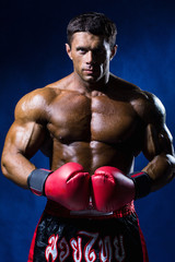 Strong muscular boxer in red boxing gloves on a blue background.