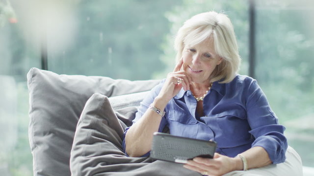 Attractive mature woman with computer tablet browsing the internet at home