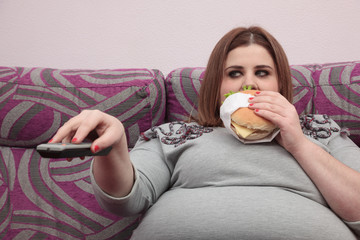 Overweight woman eating a burger and watching tv