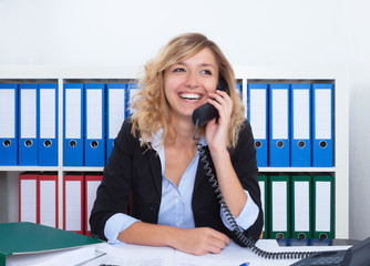 Frau mit blonden Locken im Büro flirtet am Telefon