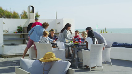 Happy group of family and friends enjoy a meal outdoors at luxury beachside home