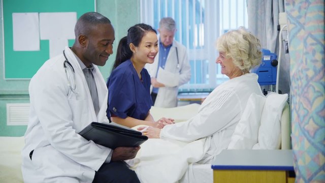 Caring doctor and nurse chatting with an elderly female patient at her bedside