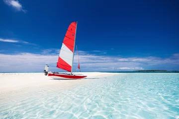 Segelboot mit rotem Segel an einem Strand einer einsamen tropischen Insel © Martin Valigursky