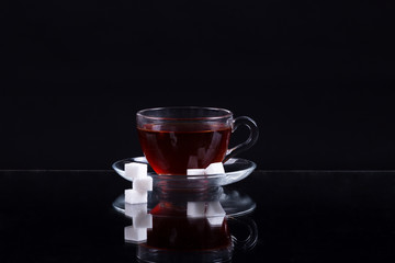 cup of black tea with slices of sugar on a black background