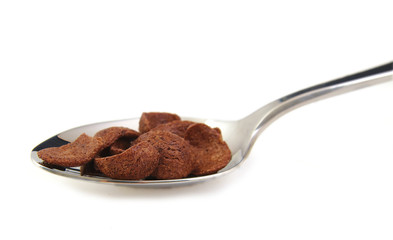 Chocolate cereals on metal spoon, white background