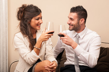 Elegant young couple drinking a toast with a glass of wine sit o