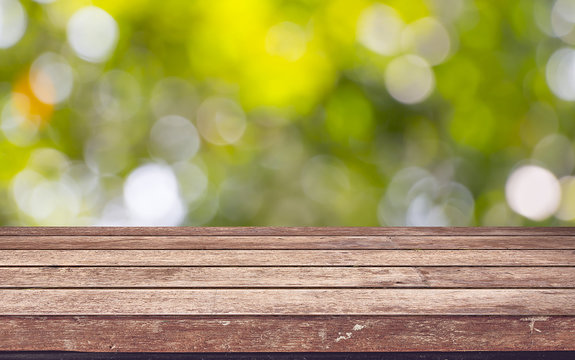 Empty wooden deck table with foliage bokeh background.