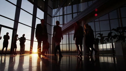 Business people walking through a modern office building at sunset - Powered by Adobe