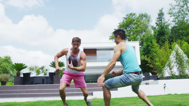 Athletic group of male friends play football in the garden of contemporary home