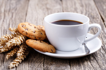 Cup of coffee with cookies and wheat on a table.