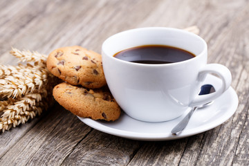 Cup of coffee with cookies and wheat on a table.