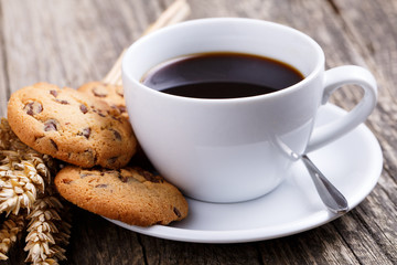 Cup of coffee with cookies and wheat on a table.