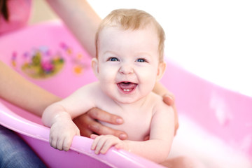 Mother washing a smiling baby in pink bathtub
