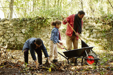 Family raking and scooping up leaves in autumn
