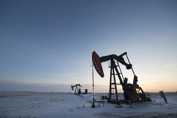 An oil drilling rig and pumpjack on a flat plain in the Canadian oil fields at sunset.  