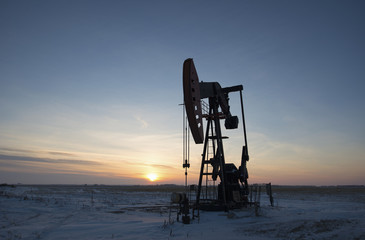 An oil drilling rig and pumpjack on a flat plain in the Canadian oil fields at sunset.  