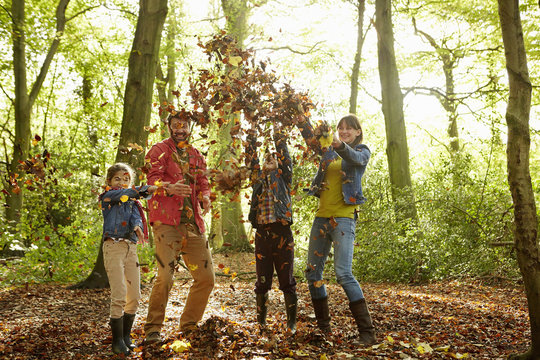 A family throwing dried leaves into the air in the woods in autumn. 
