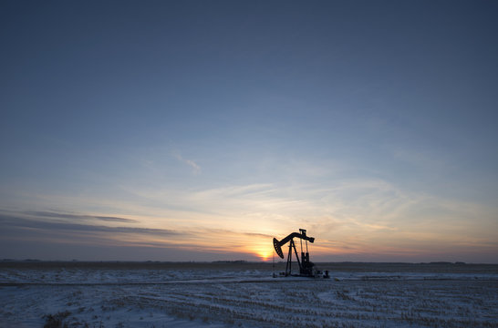 An oil drilling rig and pumpjack on a flat plain in the Canadian oil fields at sunset.  