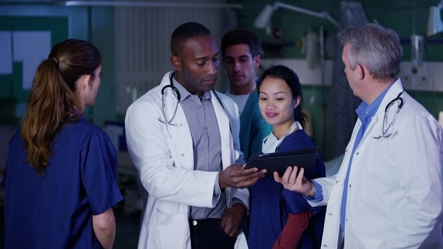 Hospital doctor with computer tablet has a discussion with other medical staff.