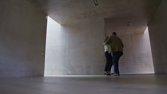 Sexy mature couple walking through modern concrete building stop to share a kiss