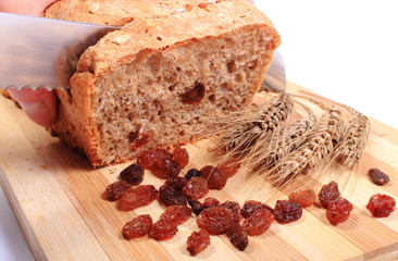 Slicing fresh bread, ears of wheat and raisins