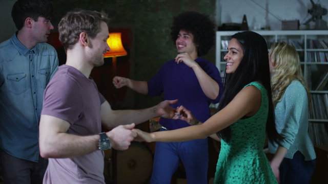 Happy and carefree group of young friends dancing and flirting at a house party