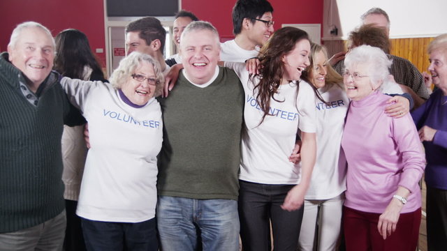 Large group of charity volunteers embrace and give big smiles into camera 