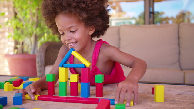 Happy little Afro girl playing with colorful building blocks
