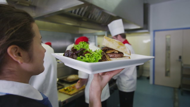 Delicious gourmet burger is prepared by the chef and taken away by the waitress