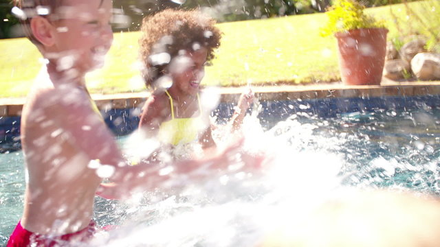 Laughing little Afro girl splashing with friends in a pool
