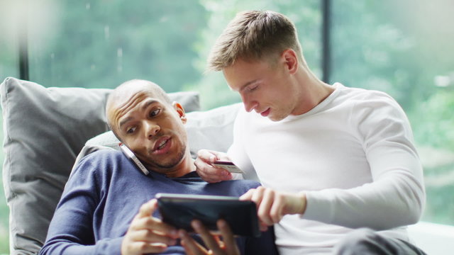 Attractive young gay couple with technology shopping on the internet at home