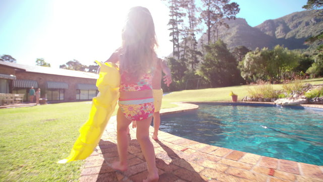 Children running with lilo towards swimming pool