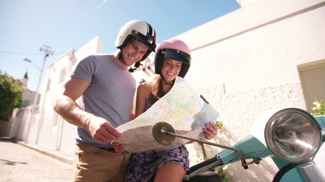 Couple discussing directions on a map next to their scooter