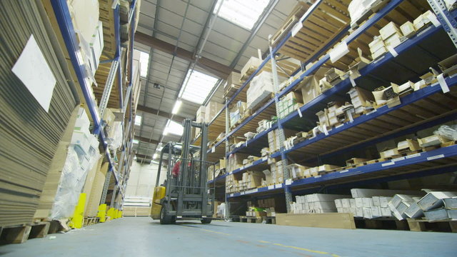 Forklift truck driver in a factory or warehouse driving between rows of shelving