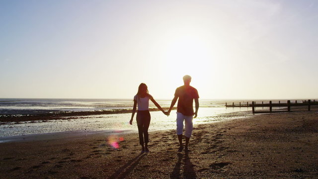 Romantic couple holding hands and walking on the beach at sunset