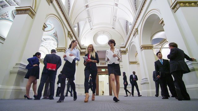 Attractive female business delegates chat as they walk through elegant building