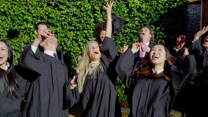 Happy multi-ethnic friends on graduation day throw their caps into the air - Powered by Adobe