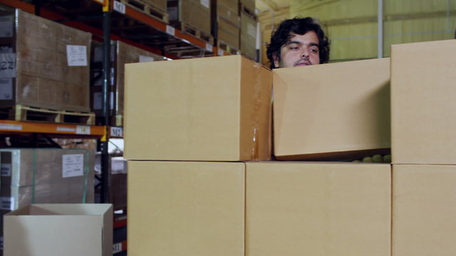 Workers in high visibility clothing are stacking plain brown boxes onto a pallet
