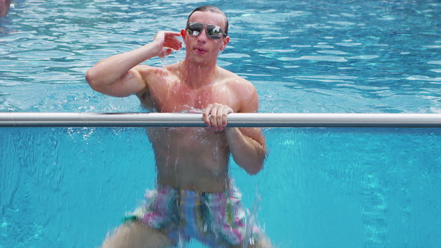 Young man with sunglasses comes up to the surface of pool with a smile  