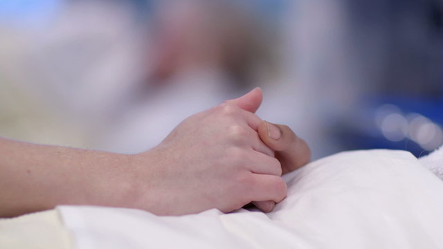 Close up holding the hand of a patient in hospital bed. No faces can be seen.