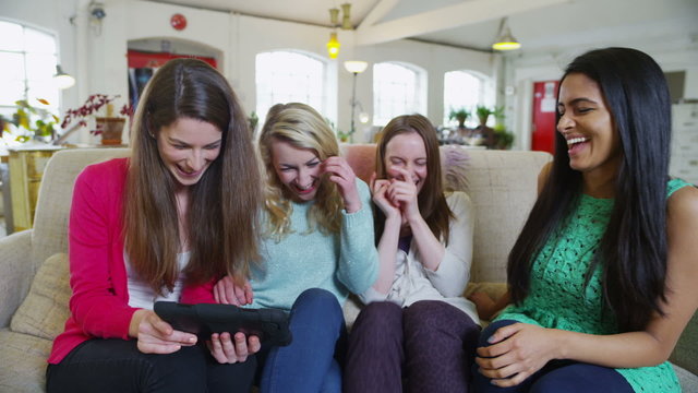 Happy casual young female friends listening to music on a tablet computer